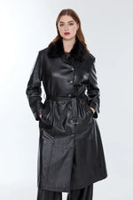 Woman wearing long black leather coat with belt and fur collar, hands in pockets